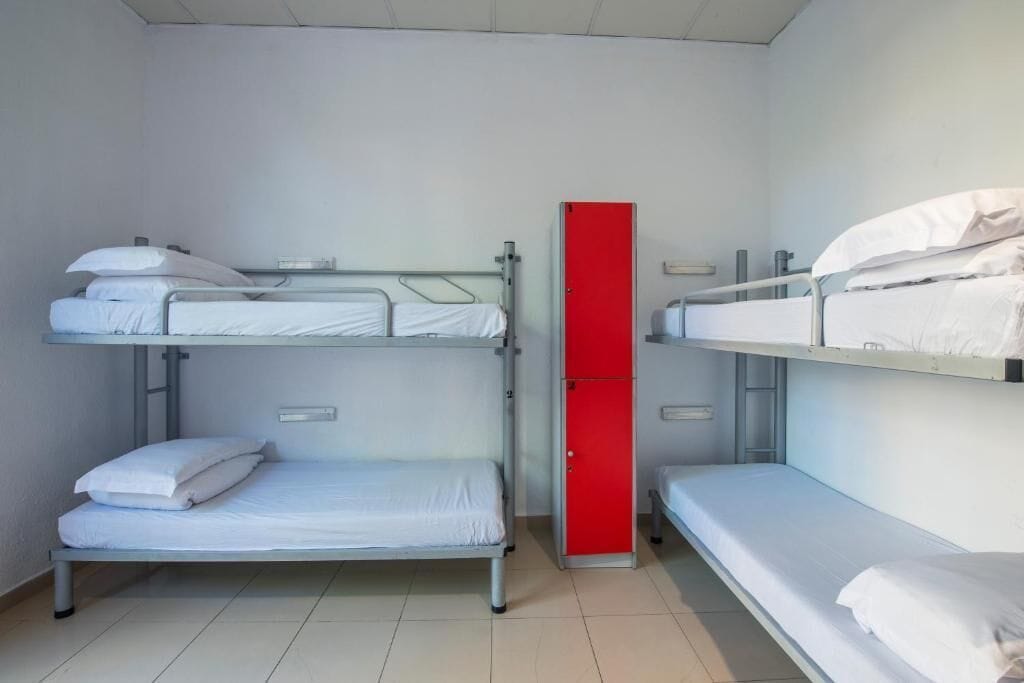 Ein Schlafsaalzimmer mit Etagenbetten, einem roten Schrank und einer weißen Wand.