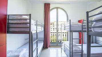Ein Schlafsaalzimmer mit Etagenbetten, einem Fenster mit Vorhängen und Blick auf Gebäude.