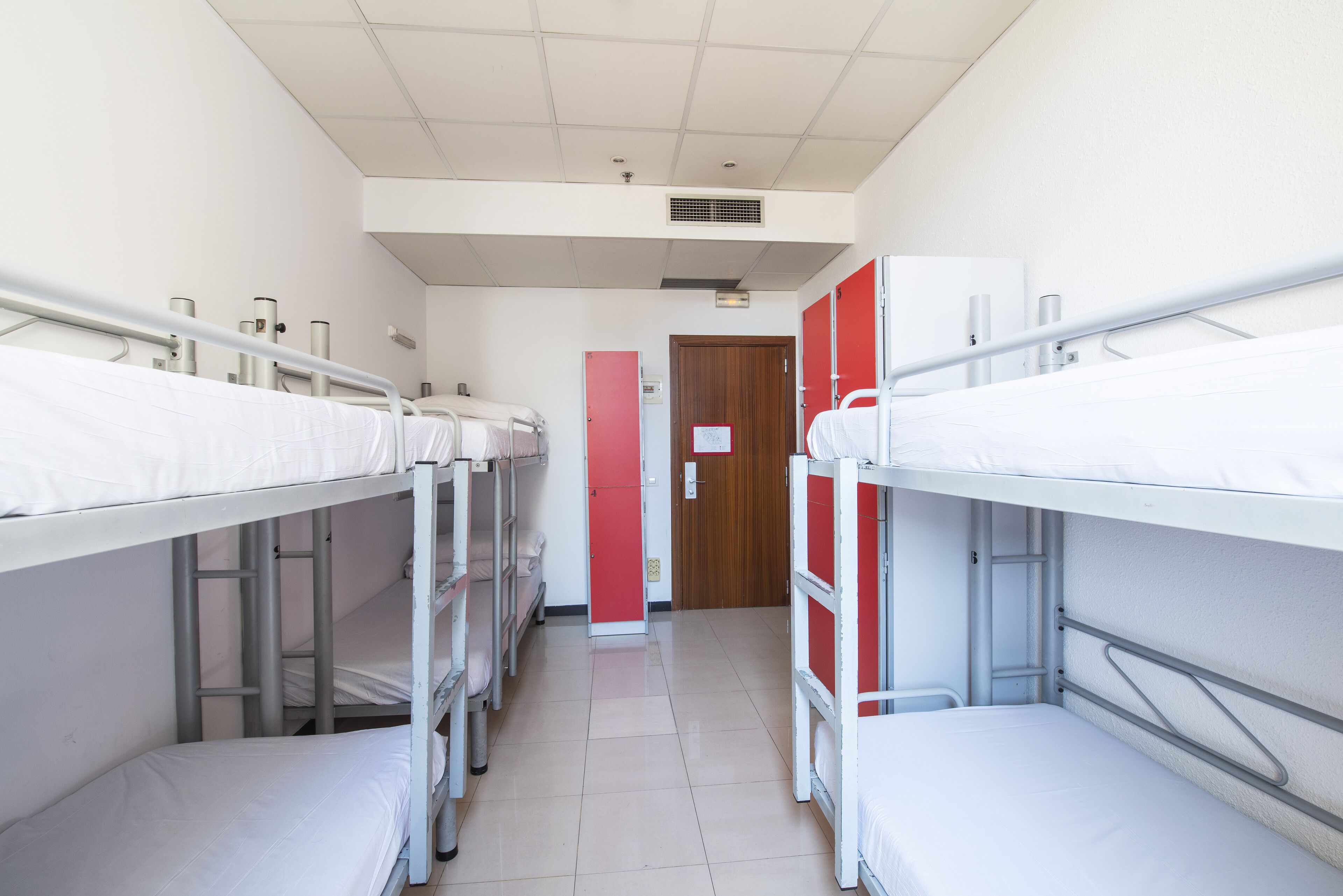 Une chambre de dortoir avec des lits superposés, une porte rouge et un sol carrelé.