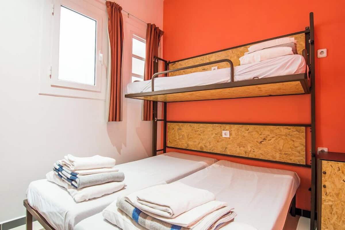 A dormitory room with bunk beds, a window with curtains, and a bed with neatly folded towels.