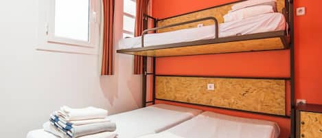 Un dormitorio con literas, una ventana con cortinas y una cama con toallas ordenadas.