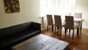 A living room with a black leather sofa, a wooden coffee table, and a dining area with four chairs and a table. - Stay.plus Budget Paradis (Bergen)
