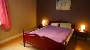 A neatly made bed with a striped blanket, two bedside tables with lamps, a painting on the wall, and a wooden floor. - Stay.plus Budget Paradis (Bergen)