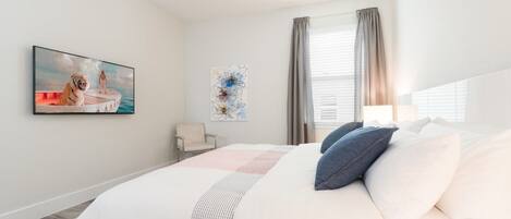 A bedroom with a large bed, a ceiling fan, a window with curtains, and artwork on the walls.