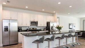 A modern kitchen with white cabinets, stainless steel appliances, and a central island with bar stools. - Je59003 - The Encore Club Resort - 9 Bed 8.5 Baths Villa (Kissimmee)