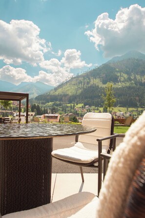 A patio with wicker furniture and a glass table overlooking a mountainous landscape. - Hotel La Soldanella (Moena)