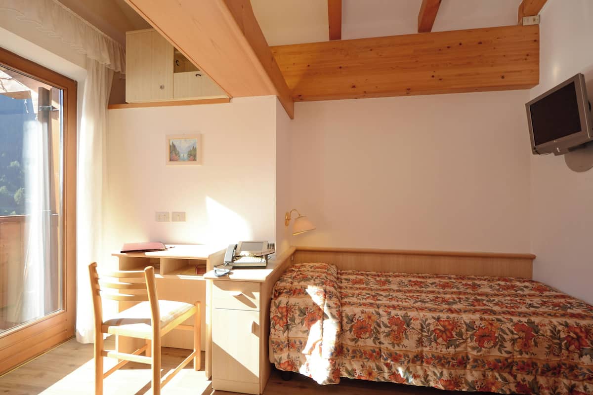 A bedroom with a wooden desk, a bed with floral bedding, a television, and a window with curtains.