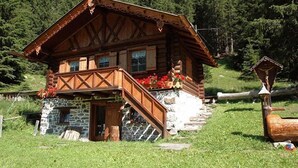 A wooden log cabin with a stone foundation, a balcony with red flowers, and a wooden staircase leading to the entrance. - Hotel La Soldanella (Moena)