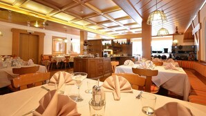 A restaurant with multiple dining areas, including a bar and a seating area with tables set for dining. - Hotel La Soldanella (Moena)