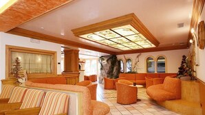 A spacious lobby with a high ceiling, a large window with a view, and multiple seating areas. - Hotel La Soldanella (Moena)