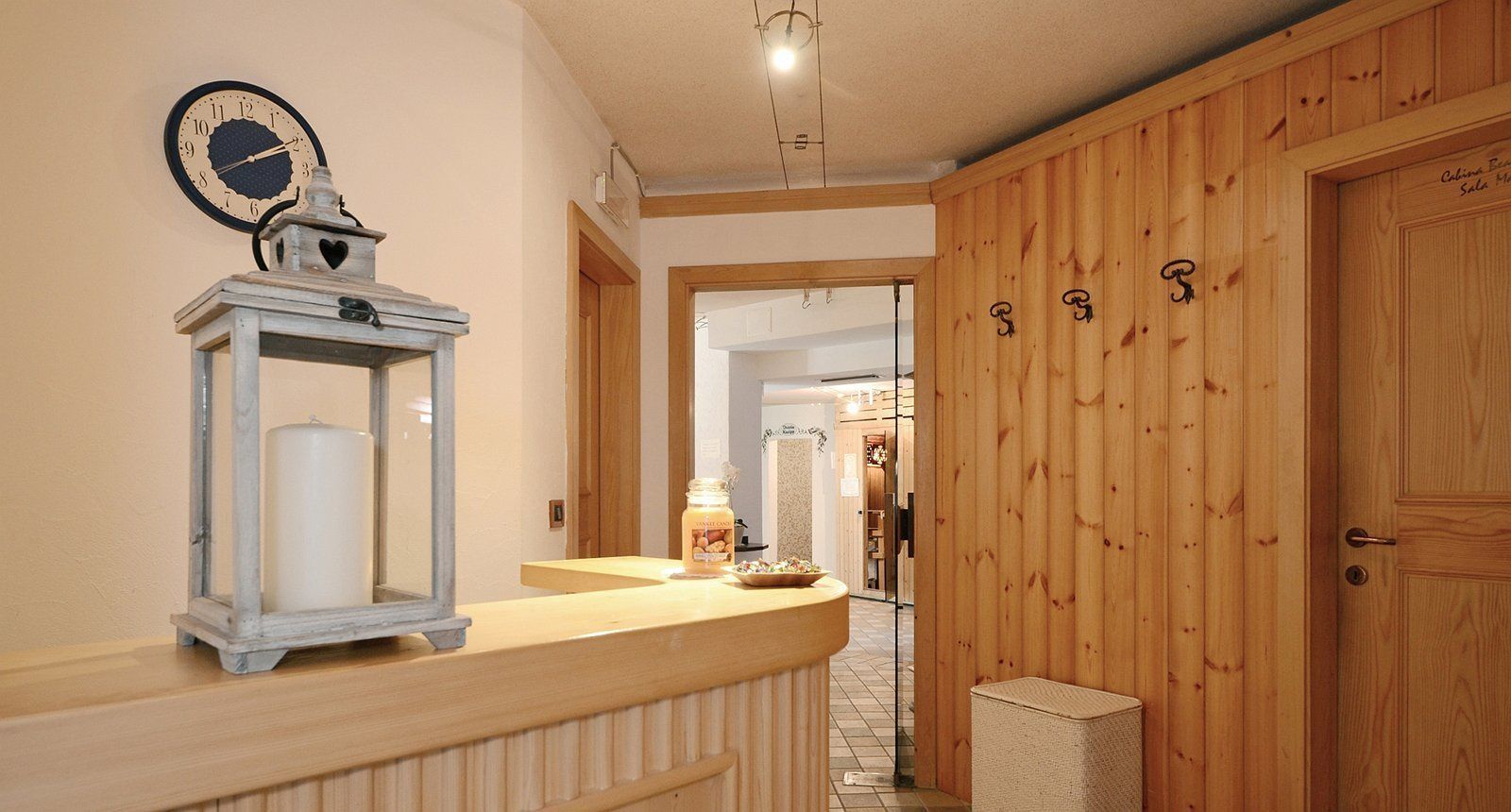 A hallway with a wooden door, a clock, and a small table with a candle and a jar.