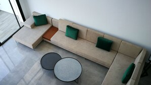 Una sala de estar moderna con un sofá seccional color beige, dos mesas de centro redondas y cojines verdes.