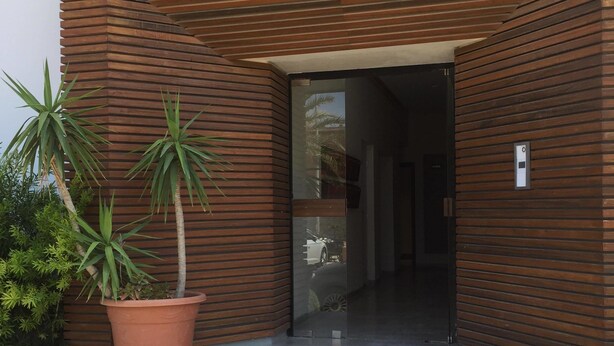 Entrada de un edificio moderno con fachada de listones de madera, una planta en maceta y una puerta de vidrio transparente.