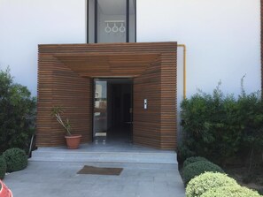 A modern building entrance with a wooden facade, a potted plant, and a small step leading to the door. - Dar Chadilia (Nabeul)