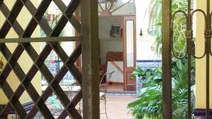 A view through a lattice gate into a courtyard with a wooden balcony, a round window, and potted plants. - Pensión Doña Trinidad (Seville)