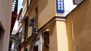 A narrow street with buildings featuring balconies and potted plants. A sign reads "Pension Dona Trinidad." - Pensión Doña Trinidad (Seville)