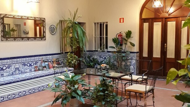 A spacious courtyard with a tiled floor, a wooden balcony, and a dining area with chairs and a table. - Pensión Doña Trinidad (Seville)