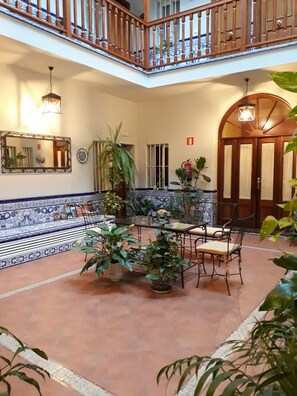 A spacious courtyard with a tiled floor, a wooden balcony, and a dining area with chairs and a table. - Pensión Doña Trinidad (Seville)