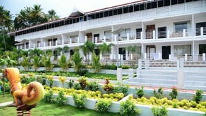 Un hotel de varios pisos con balcones, un jardín bien cuidado con diversas plantas y una escultura decorativa de un caballo.