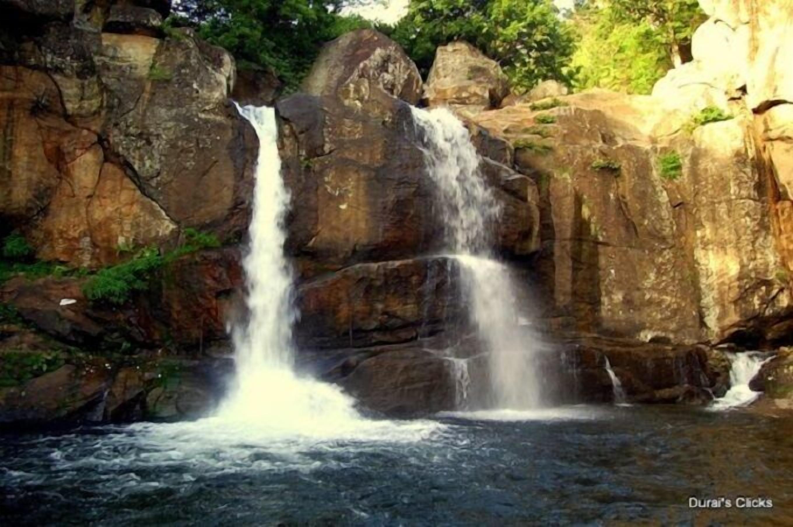 Una cascada que se precipita sobre terreno rocoso, rodeada de abundante vegetación.