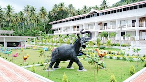 Un hotel con una gran estatua de elefante en el patio, rodeado de palmeras y coloridas estructuras de juego.