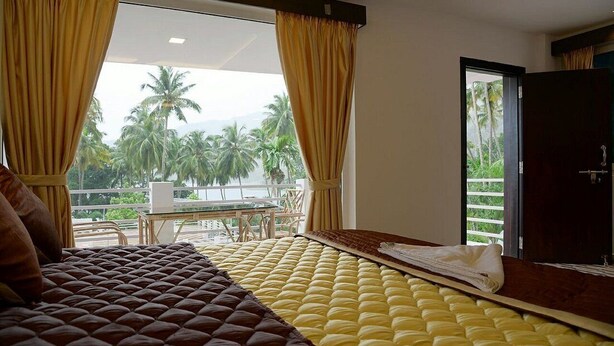 Habitación de hotel con una cama, vista a palmeras y un balcón con mesa y sillas.