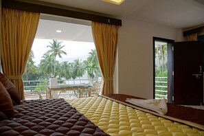 A hotel room with a bed, a view of palm trees, and a balcony with a table and chairs. - Orchard Valley Resort (Shenkottai)