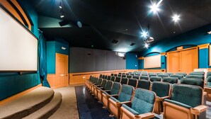Ein Theater mit Reihen grüner Sitze, einer Bühne mit Teppichboden und einer Ausgangstür.