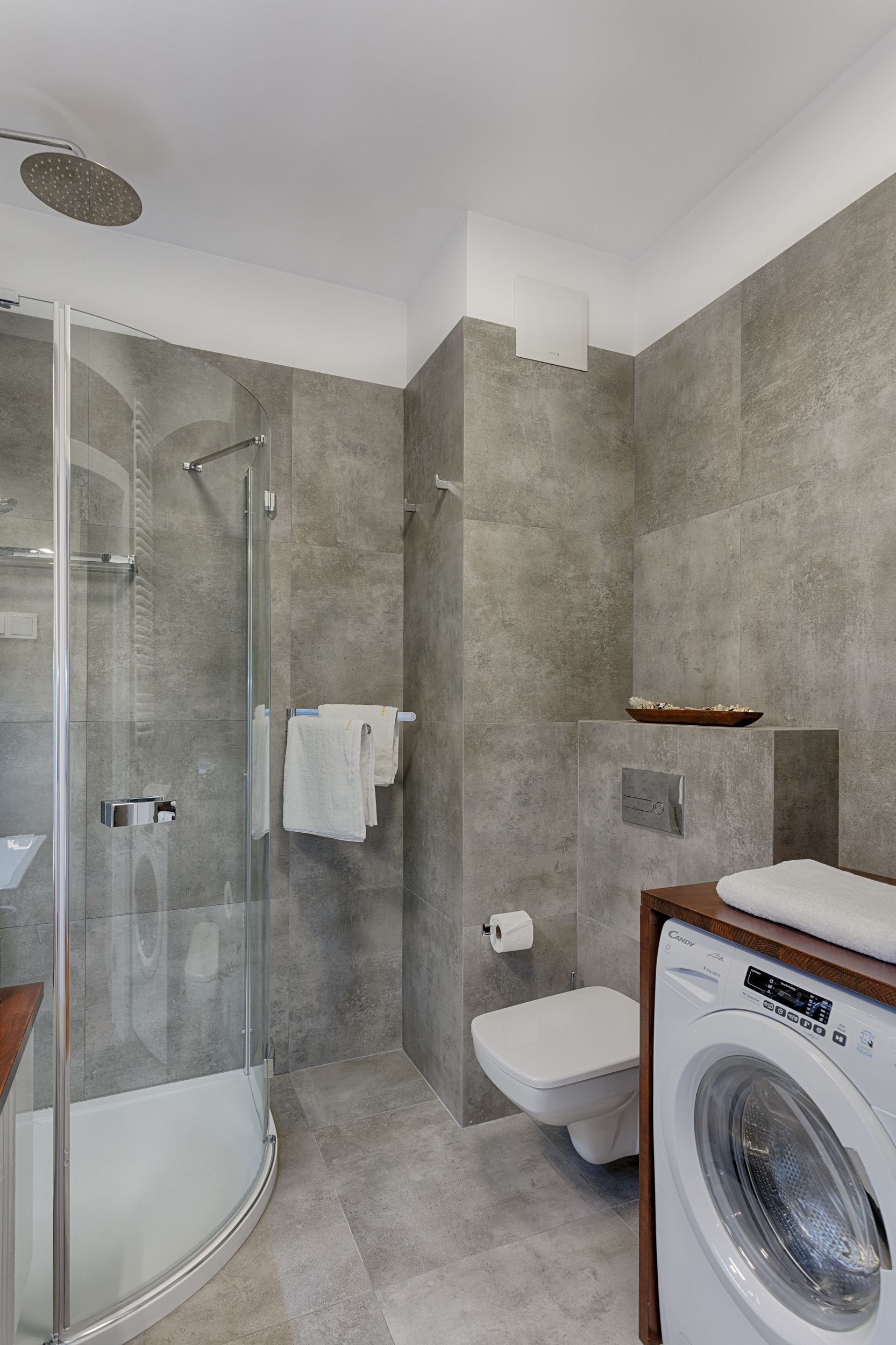 A modern bathroom with a glass-enclosed shower, a toilet, and a built-in washing machine.