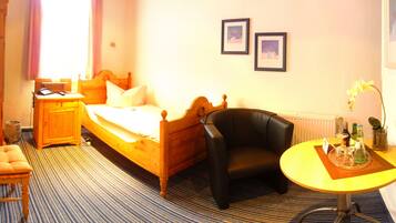 A hotel room with a wooden bed, a black leather chair, a small round table with a vase of flowers, and two framed pictures on the wall.