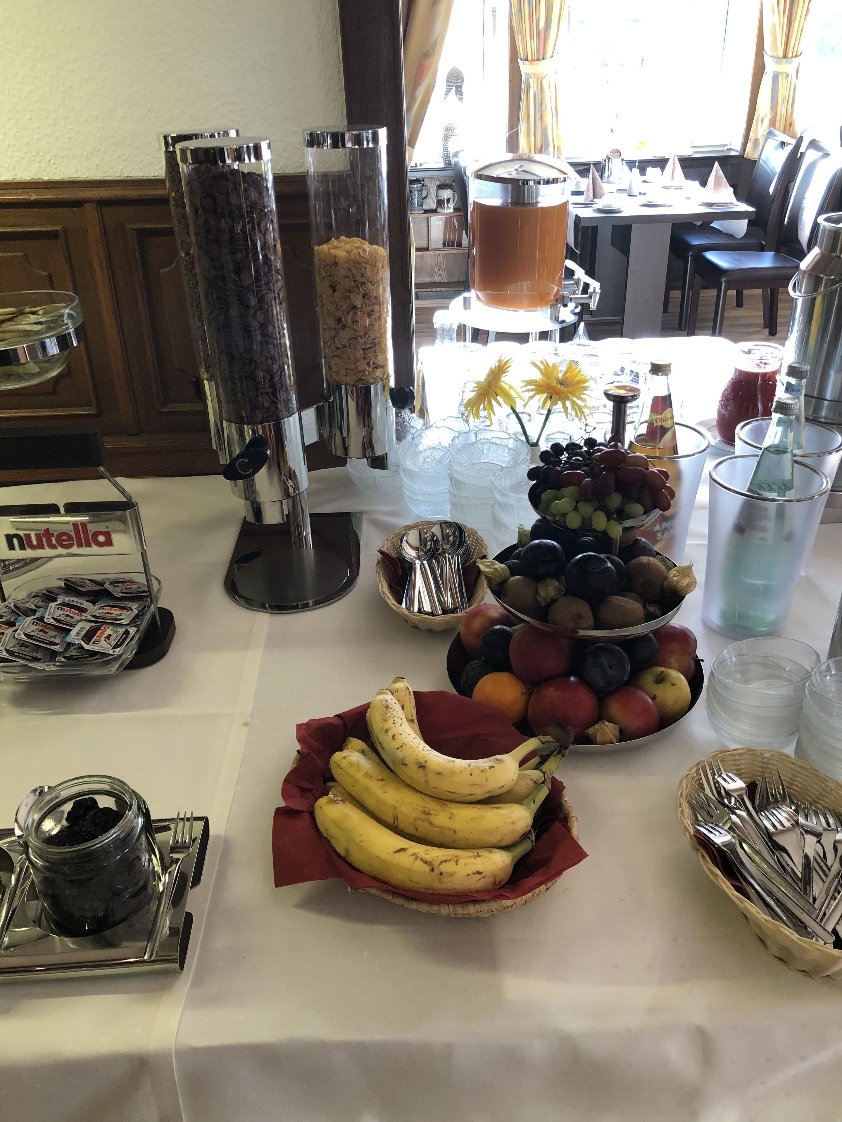 A buffet table with various food items, including bananas, grapes, and a bowl of apples.