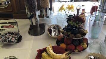 A buffet table with various food items, including bananas, grapes, and a bowl of apples.