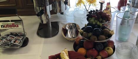 Een buffettafel met diverse etenswaren, waaronder bananen, druiven en een schaal appels.