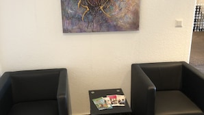 Un área de recepción con dos sillones de cuero negro, una pequeña mesa con folletos y un cuadro abstracto grande en la pared.