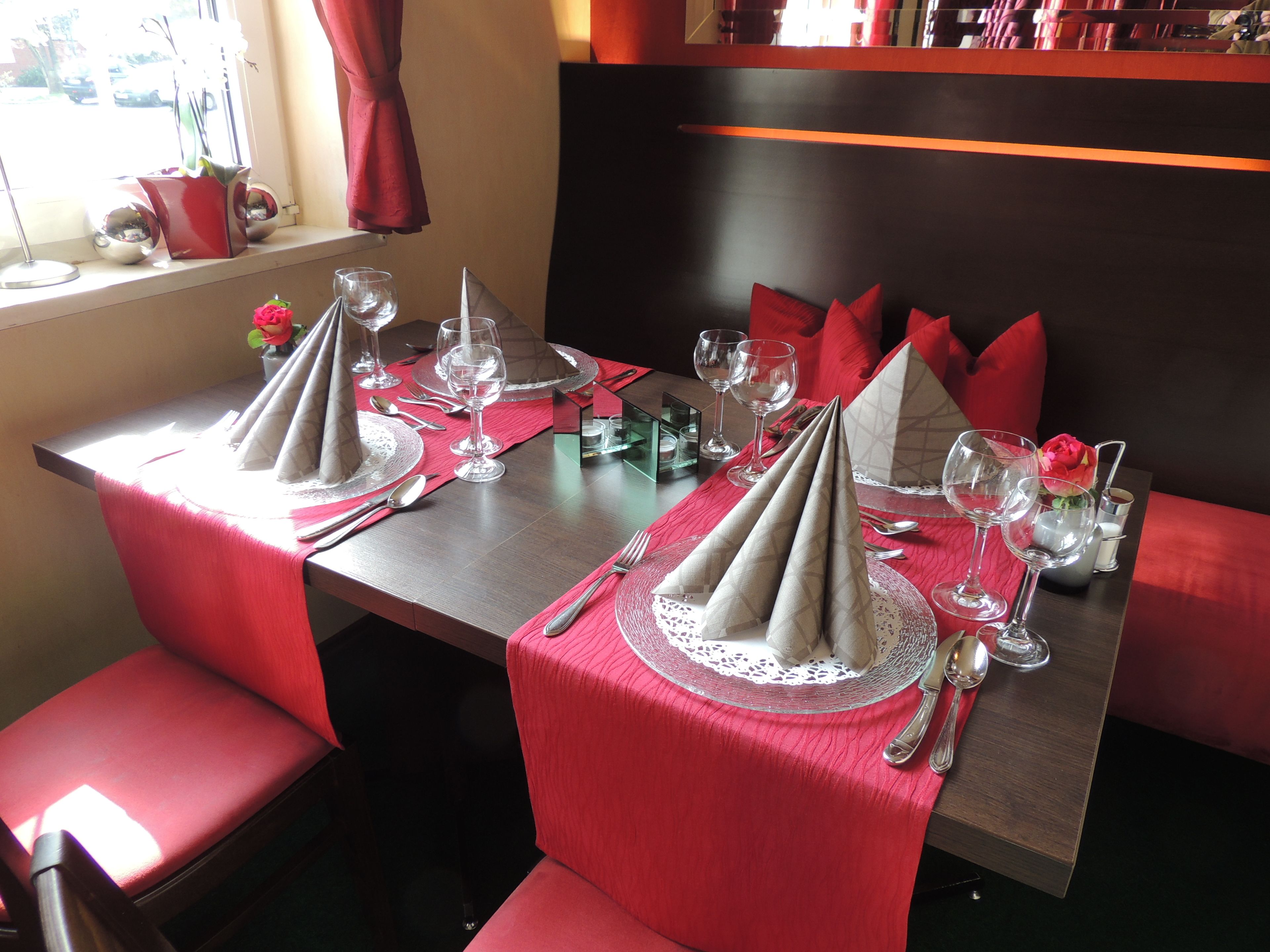 A dining table set for two with red napkins, silverware, and wine glasses.