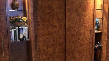 A wardrobe with a 'Garderobe' sign, shelves with books and a vase, and a tiled floor.