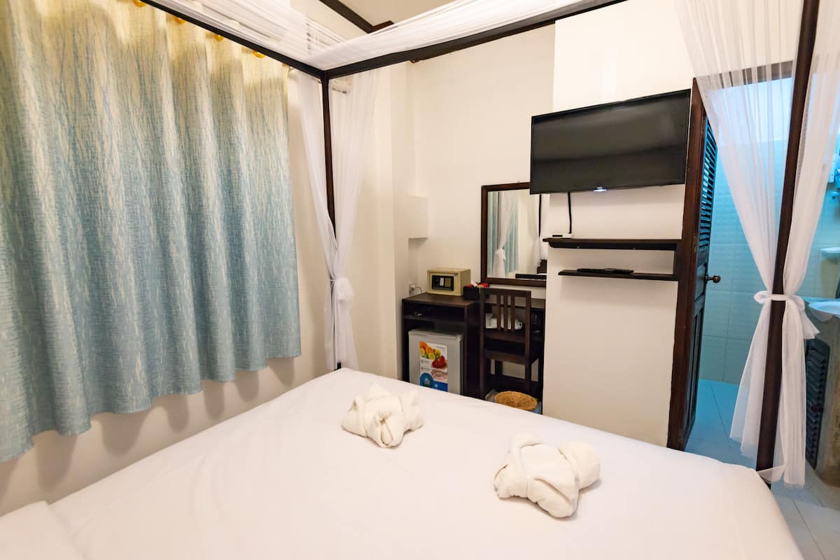 A hotel room with a bed, a TV mounted on the wall, a small desk with a chair, and a bathroom visible through a door.