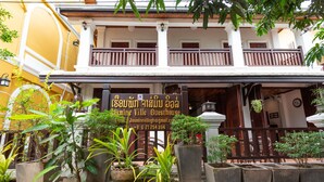 A guesthouse with a signboard, potted plants, and a balcony.