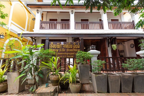 A guesthouse with a signboard, potted plants, and a balcony.