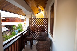 Ein Balkon mit Korbmöbeln, einem Holzziergitter und Blick auf Gebäude und Grünflächen.