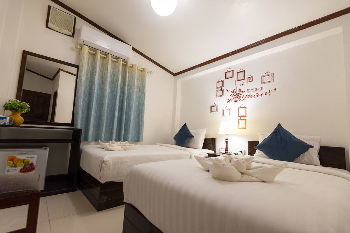 A hotel room with two beds, a desk with a refrigerator, a mirror, and a wall with decorative elements.