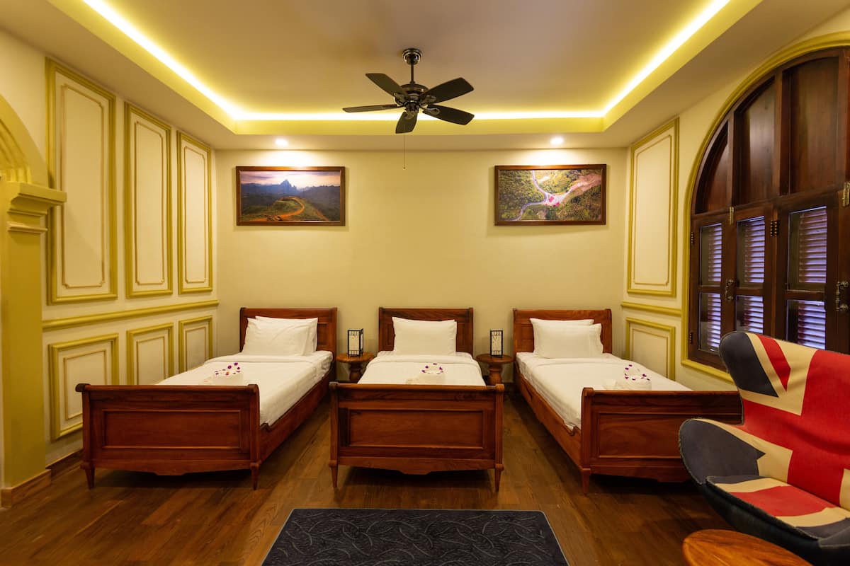 A hotel room with three wooden beds, a ceiling fan, and two wall-mounted lamps.