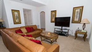 A living room with a brown leather sofa, a round coffee table, a flat-screen TV, and framed artwork on the walls. - Ahr205 - Highgate at Legacy Park - 5 Bed 4 Baths Villa (Davenport)