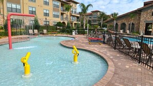A swimming pool with two yellow water features, surrounded by lounge chairs and a brick walkway.