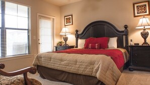 A bedroom with a large bed, two bedside tables with lamps, a chair, and a window with blinds.