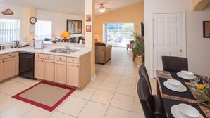 A spacious kitchen with a central island, a dining area with a table set for four, and a living room with a couch and a large window. - Ip60283 - Rolling Hills Estates - 4 Bed 3 Baths Villa (Kissimmee)
