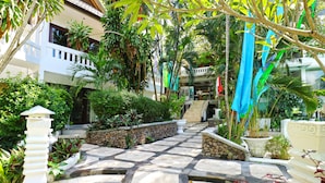 A courtyard with a stone pathway, potted plants, and a building with a balcony. - Bali Mystique Apartment (Keroboken Kelod)