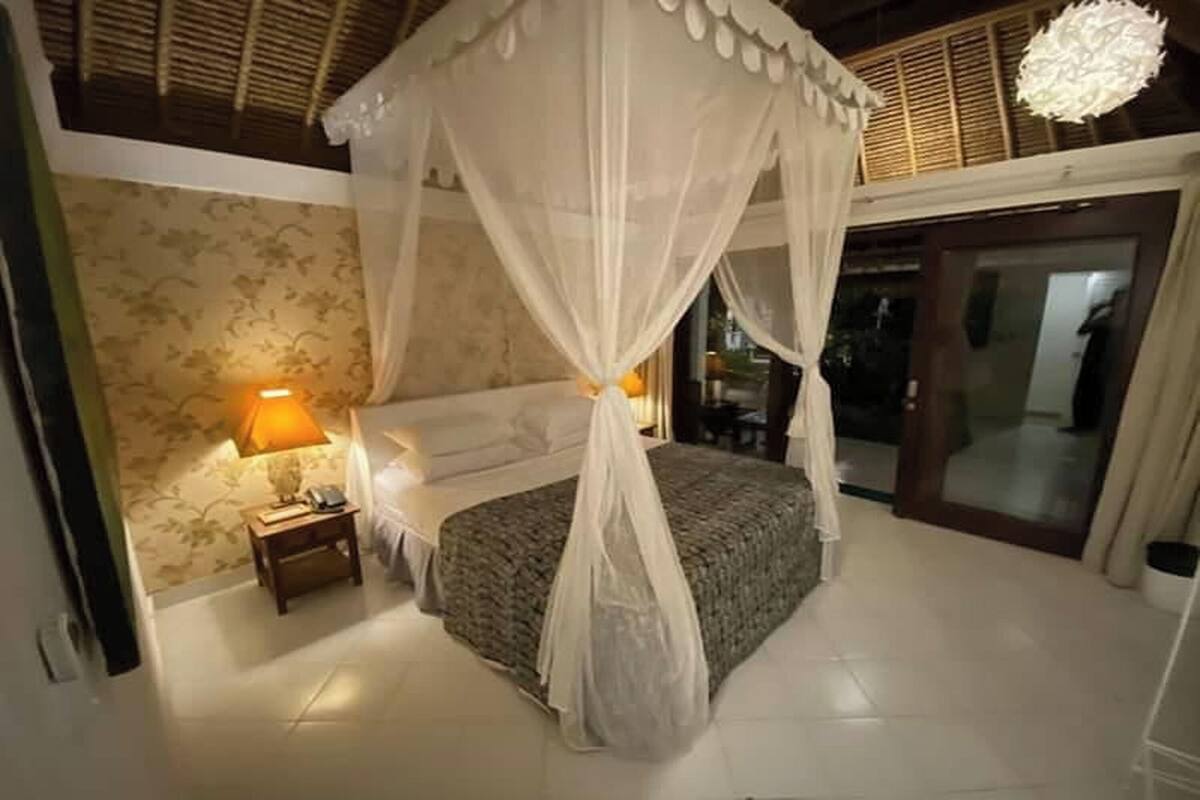 A bedroom with a canopy bed, a nightstand with a lamp, and a patterned wall.