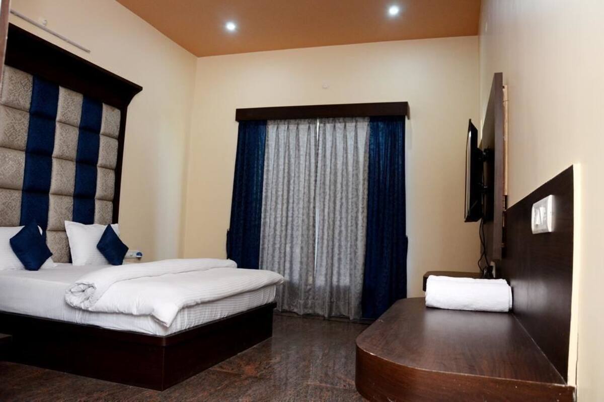 Une chambre d’hôtel avec un lit, une table de chevet, une télévision et une fenêtre avec des rideaux.