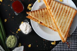 Ein gegrilltes Sandwich auf einem Teller, mit Beilagen und Maiskörnern auf einer dunklen Oberfläche.